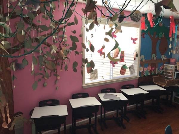 Preschool classroom with individual desks and a nature-themed learning area